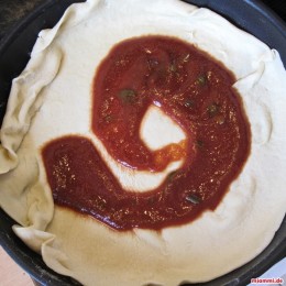Etwas Olivenöl in die Pfanne geben und den Teig vorsichtig in die Pfanne legen. Auf dem Pizzateig die Tomatensoße in der Pfanne verstreichen.