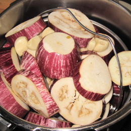 Einen Topf zu etwa einem Drittel mit Wasser füllen und einen metallenen Sieb zum Gemüsekochen in den Topf legen, so dass das Gemüse nur mit dem Dampf gegart wird. Hinein legen wir die Auberginen und die Knoblauchzehen, damit diese schön weich werden. Wir haben den Schnellkochtopf genommen und das Gemüse für knappe 20 min auf Stufe 2 kochen lassen.