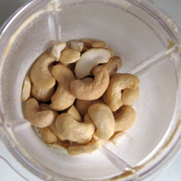 Cashews mit 50 ml Wasser, der Knoblauchzehe und einer Scheibe Zitrone in einem kleinen Mixer zu Cashew-Joghurt mixen.
